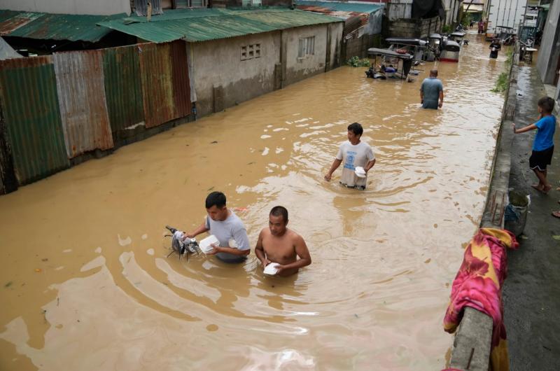 Người dân mang theo đồ ăn lội dọc con phố ngập lụt do bão Noru ở thị trấn San Miguel, tỉnh Bulacan, Philippines, ngày 26.9.2022. Ảnh: AP